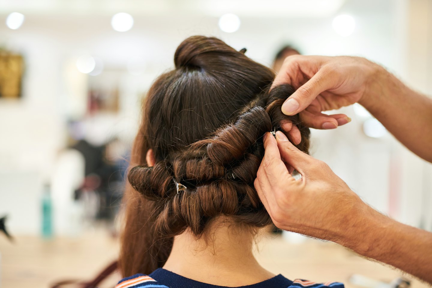 Home Mani di parrucchiere che arricciano e fissano lunghi capelli castani.