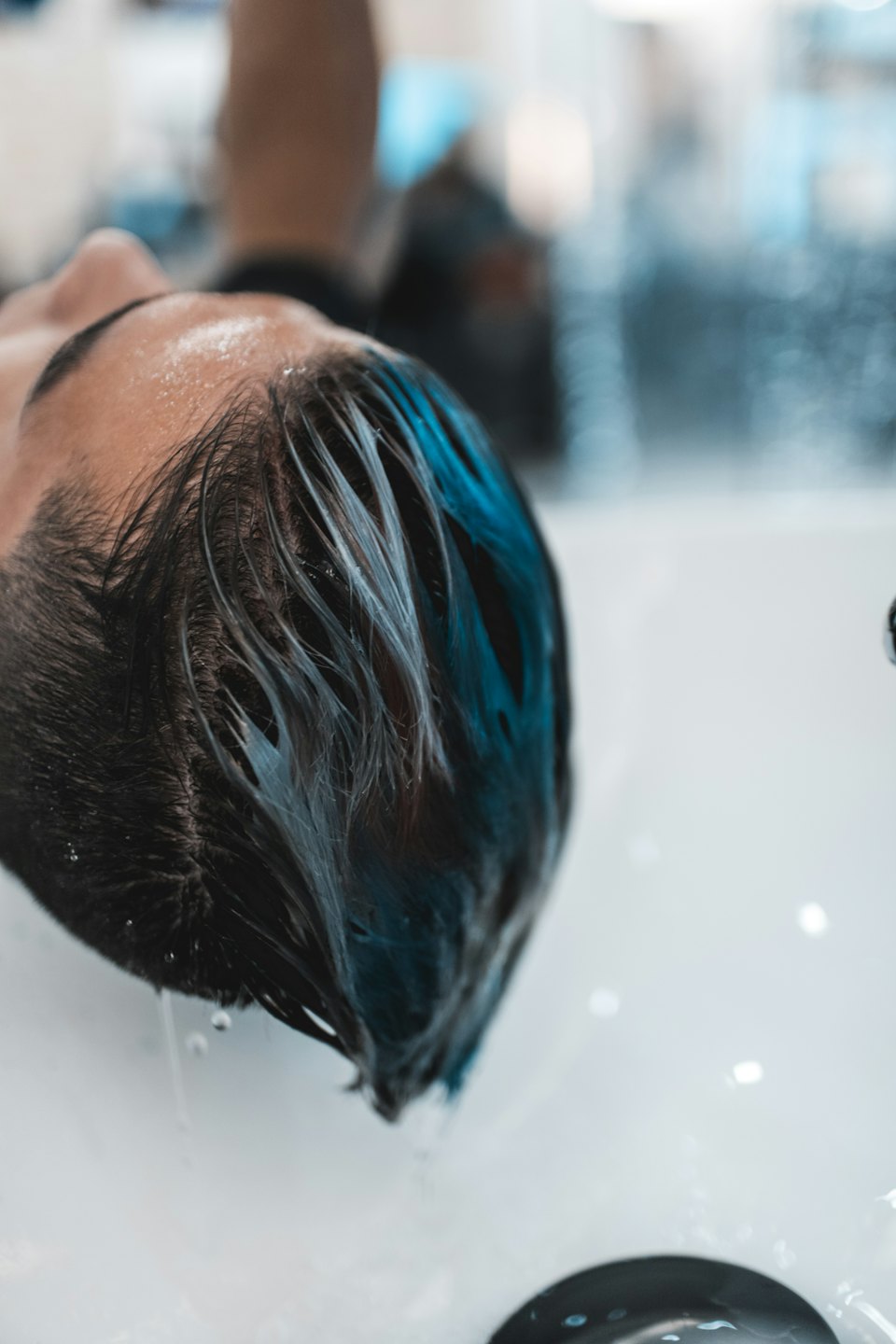Home Una parrucchiera sciacqua capelli blu e scuri nel lavatesta di un salone.