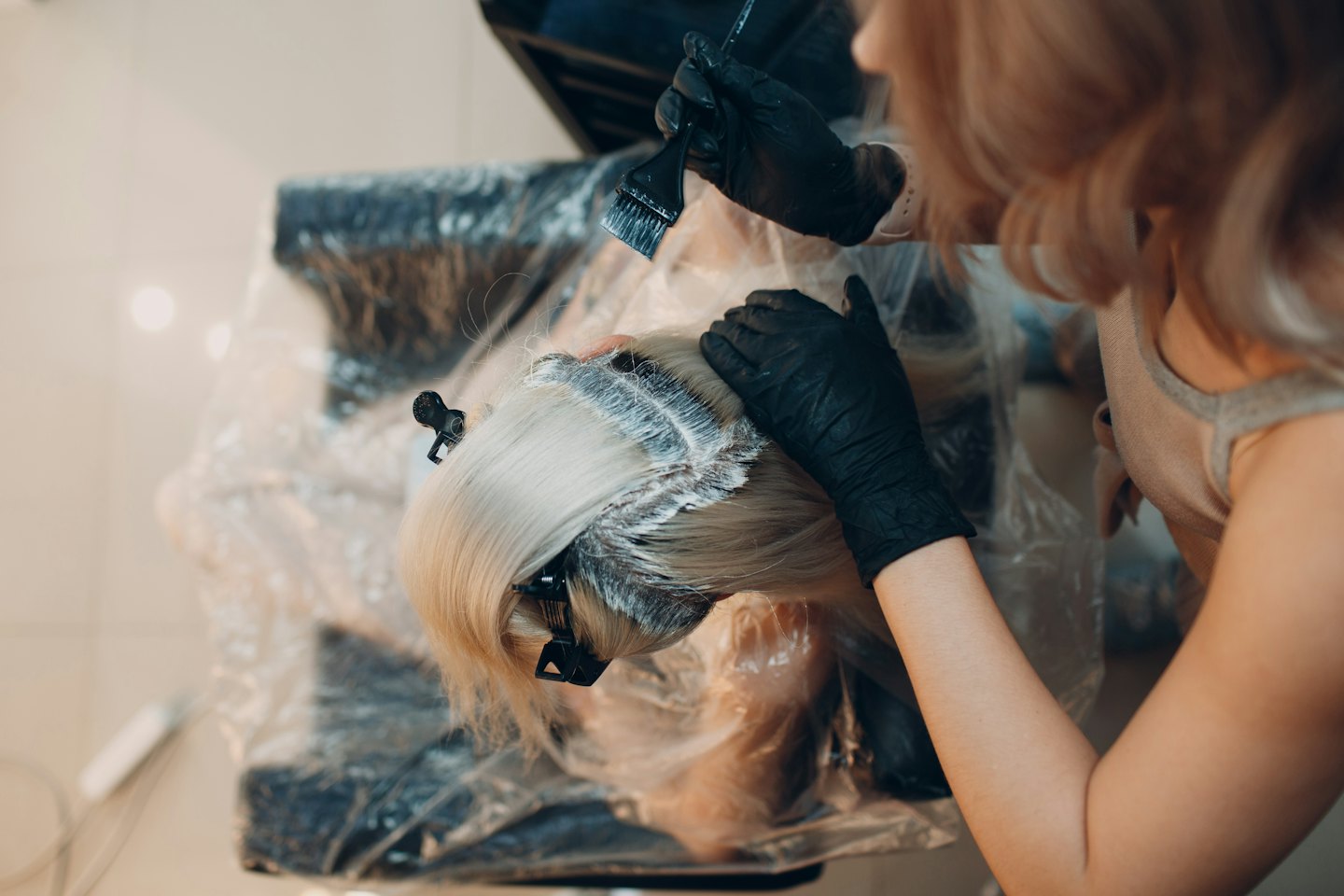 Professionista applica tinta alle radici dei capelli di una cliente in un salone.